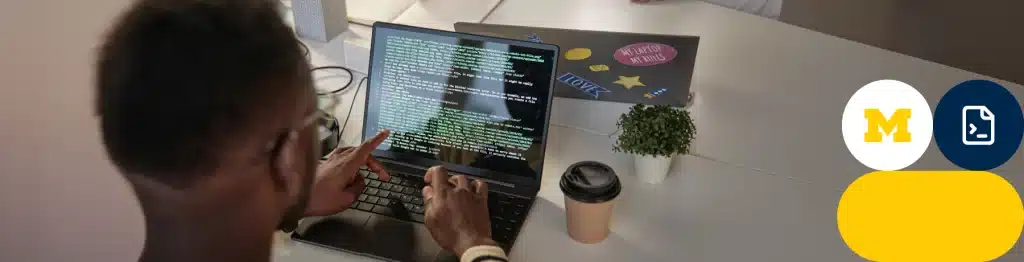 Person coding on a laptop with University of Michigan logo in the background